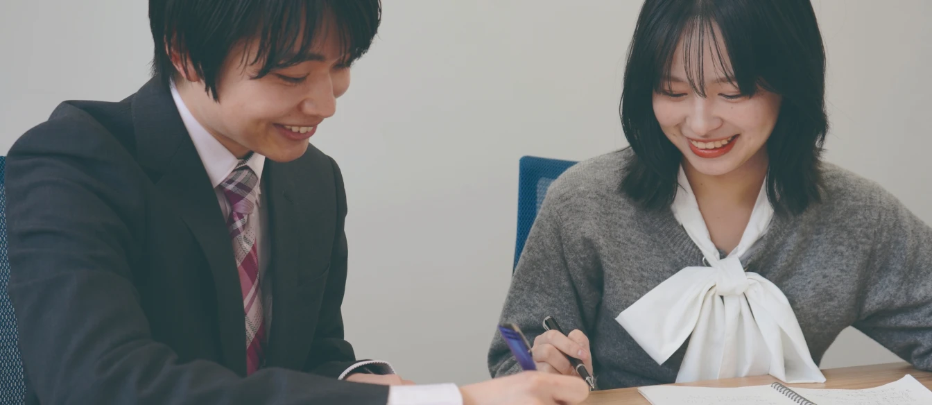 ノートにメモを取りながら打ち合わせをする笑顔の男女2人の社員