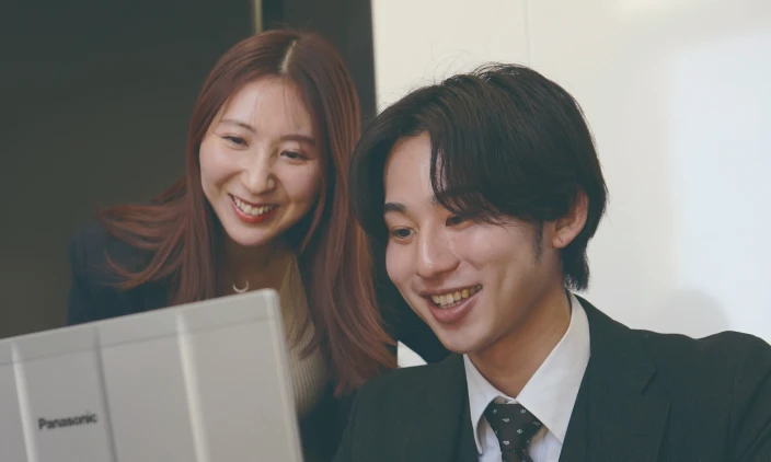 パソコン画面を見ながら笑顔で話し合う男女2人の社員