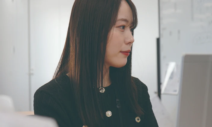 パソコン画面を横から見つめる黒いジャケットを着た女性社員