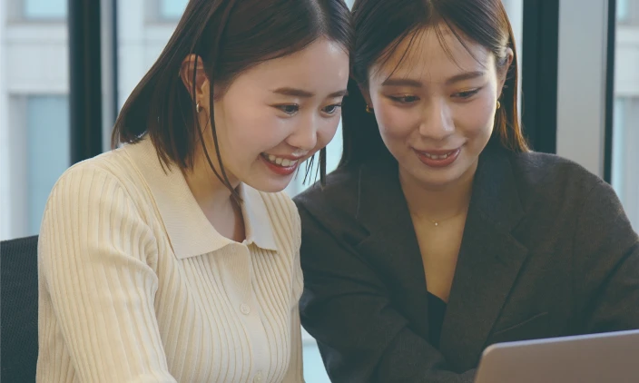 パソコン画面を見ながら笑顔で話し合う2人の女性社員