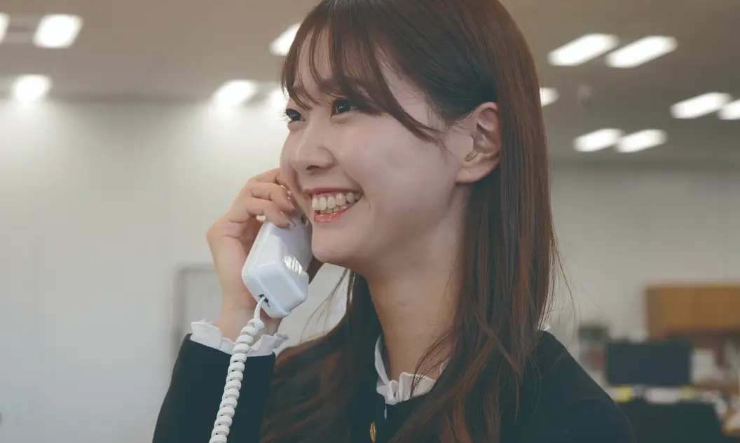 オフィスで電話対応をしながら笑顔で話す女性社員